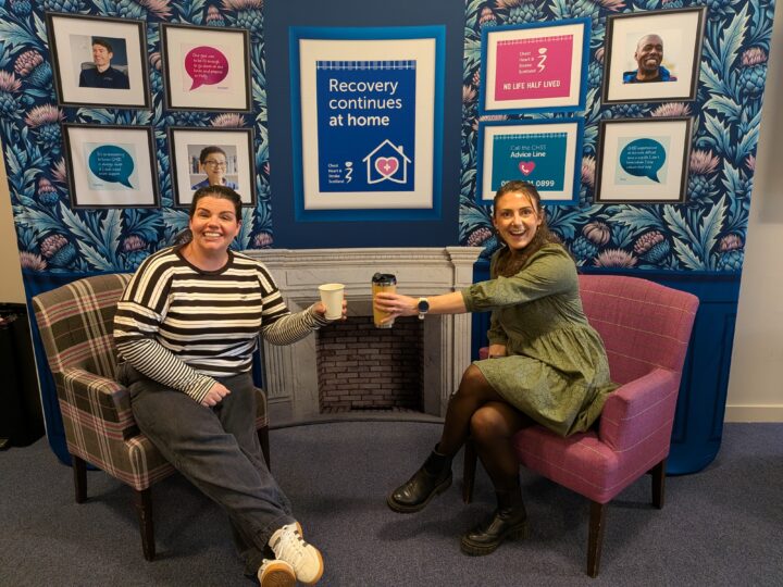 two people, sitting in armchairs toasting hot drinks with CHSS branding behind them. background