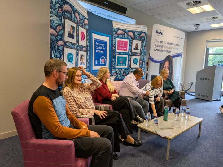 6 panellists - mid conversation in conference room.